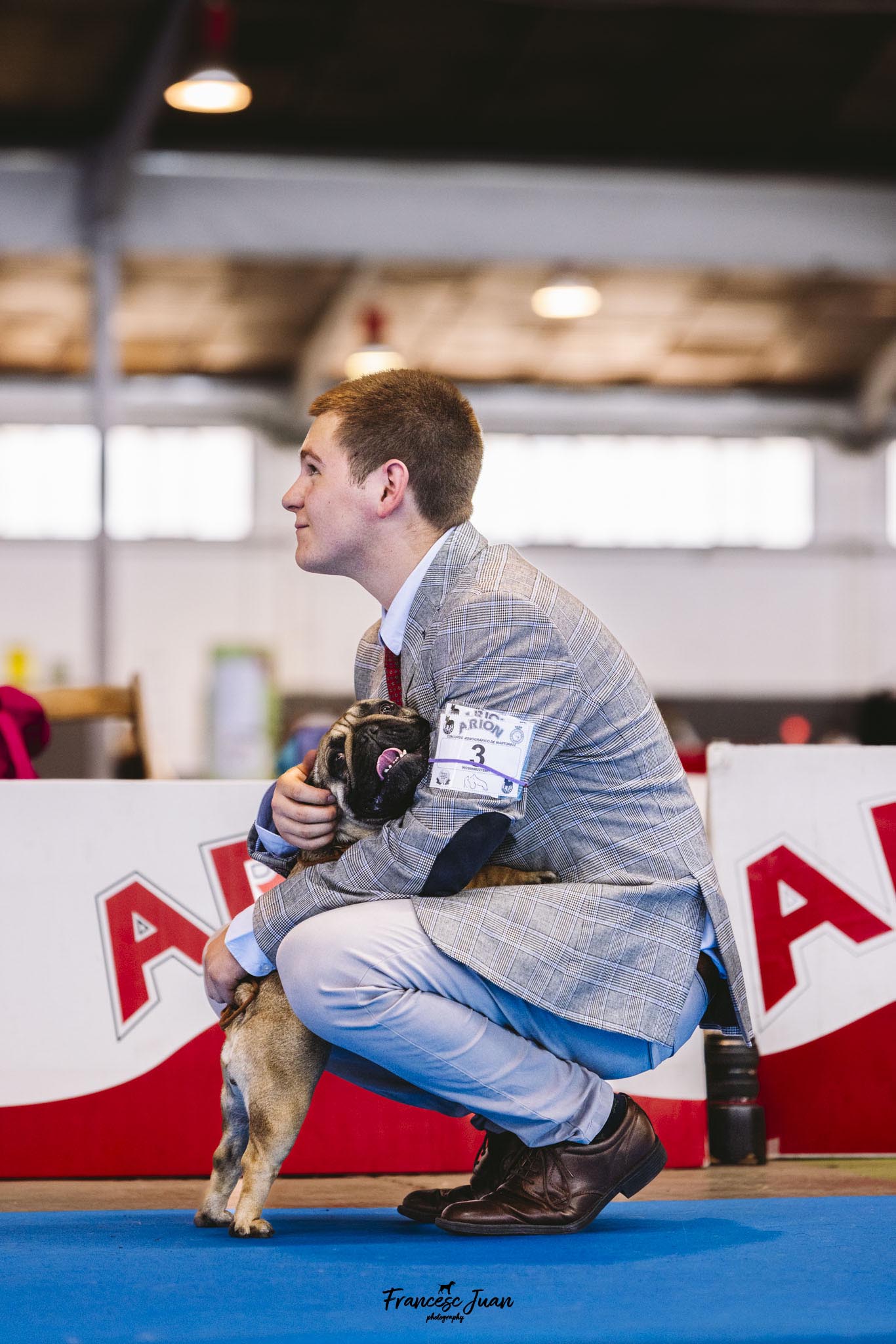 Handler joven abrazando con cariño a un perro de raza carlino durante una exposición canina